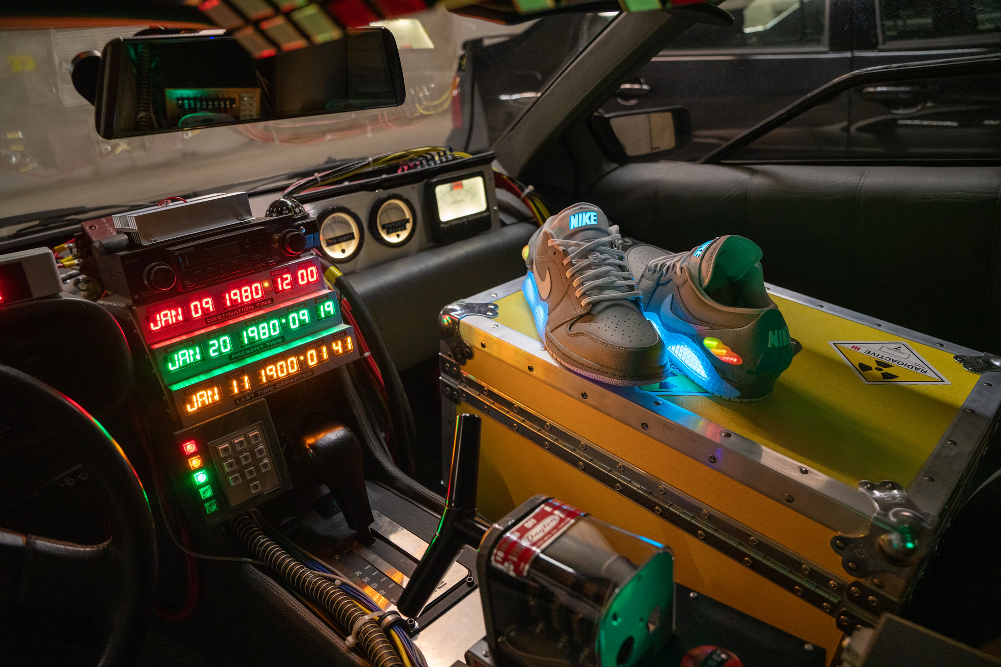 DeLorean 'Time Machine' replica interior: Time circuit switch and display, a hoverboard, plutonium case with stickers, and some custom Nike Air Jordan sneakers modified to include the blue 'Mag' cut-outs and heel caps similar to the sneakers in the second movie.
